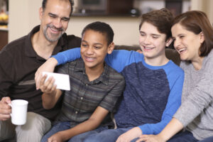 family members at home sharing memories on cell phone. couple with adopted or foster care children.