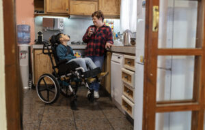 Latin mother drinking coffee in the kitchen with her disabled son. Concept of family, unconditional love and inclusion.