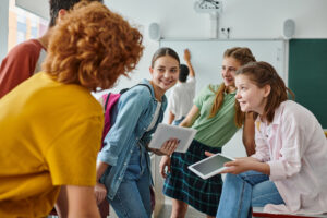 Students share smiles and excitement while collaborating with tablets in a lively classroom setting.
