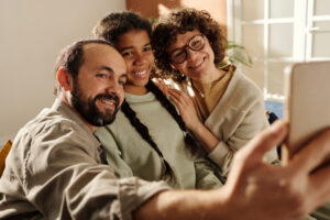 Happy family making selfie portrait on smartphone with African American adopted girl in the room at home