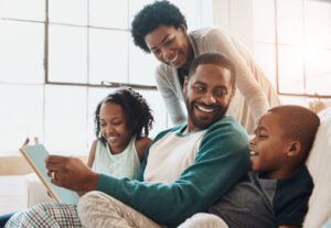 Reading, happy and black family with book on sofa for bonding together on fathers day at home. Smile, knowledge and African parents relaxing with children in living room with fantasy story or novel.