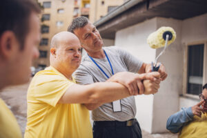Group of people, men and women with down syndrome volunteers organizing to renovate building outdoors together.