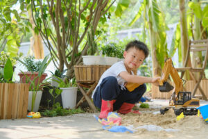 Asian smiling kid playing with sand toys and toy construction machinery in backyard home garden