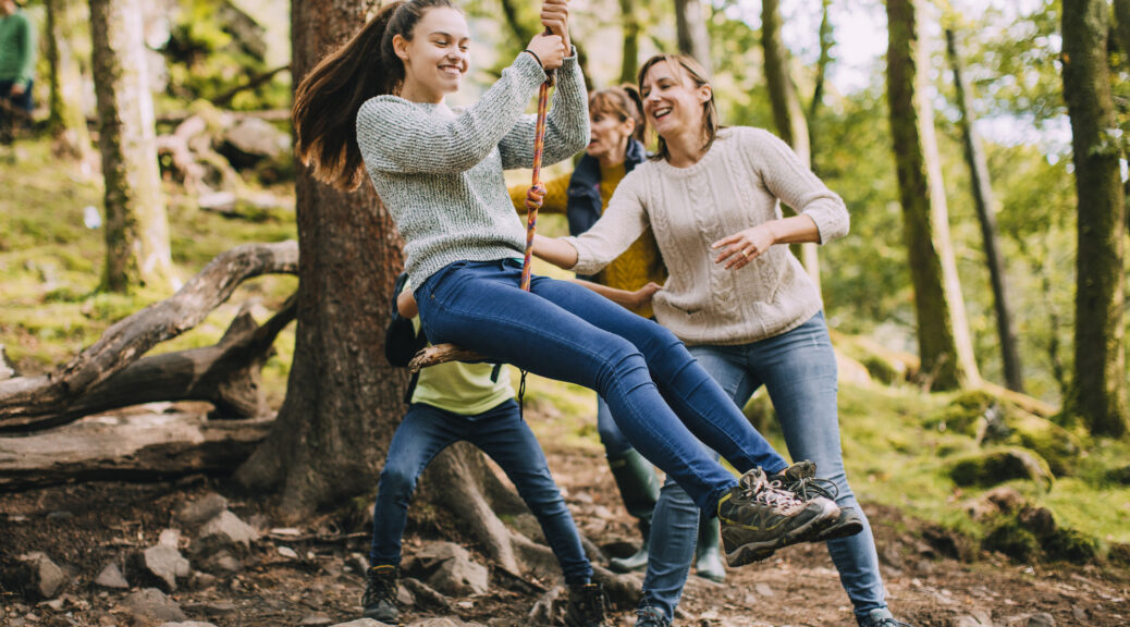 Teenage girl is being pushed on a rope swing in the woods by her family.